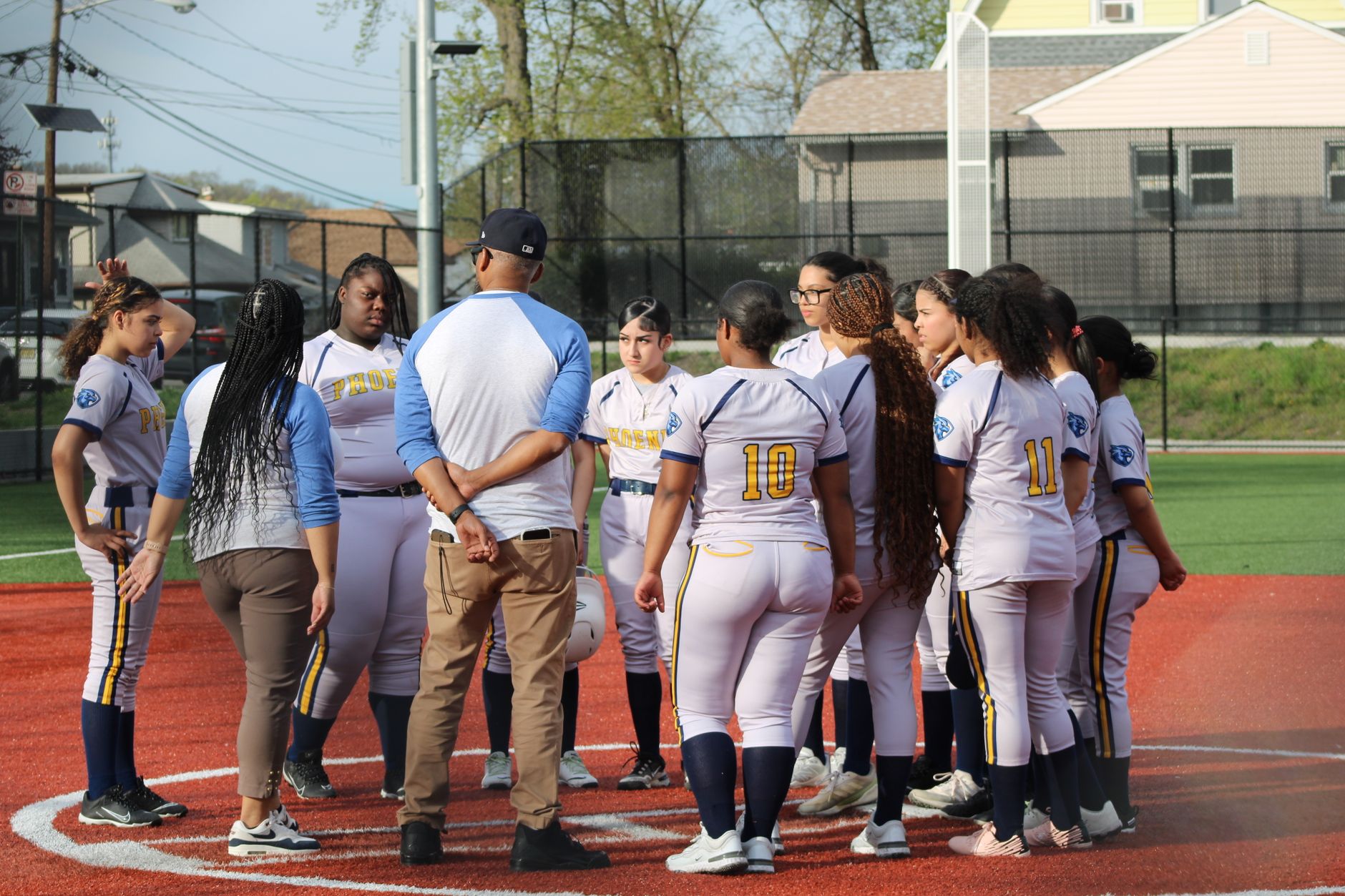A softball coach talking through strategy with the team gathered around on the field