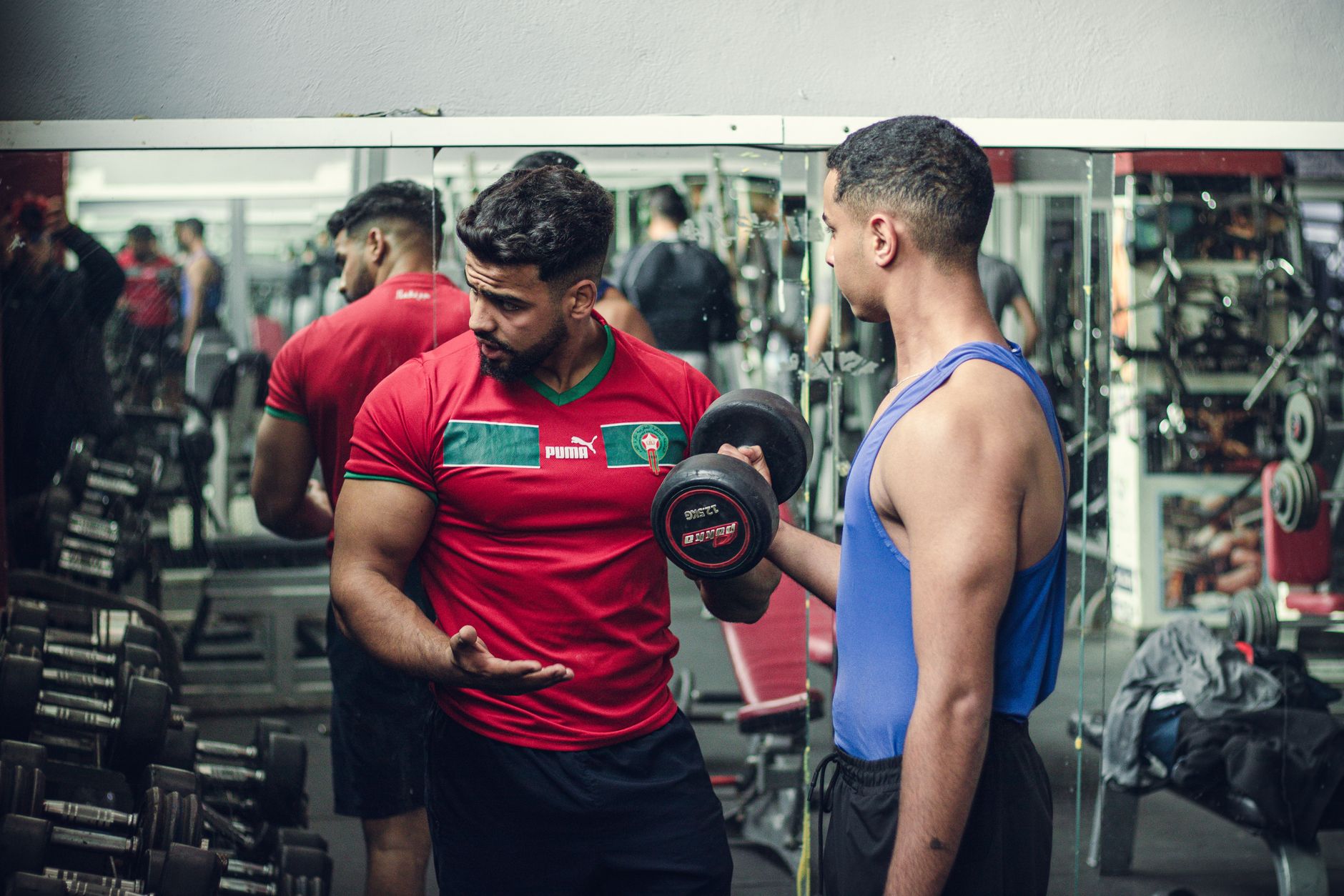 A fitness trainer correcting a client's form partway through a dumbbell set in a gym