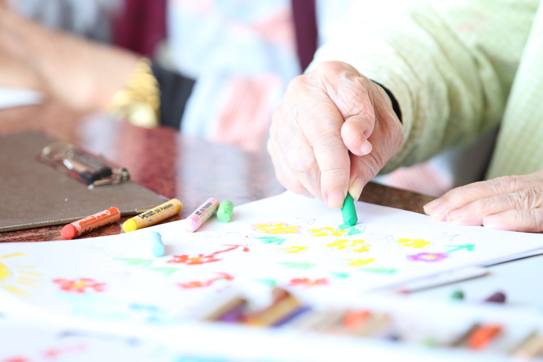 An older adult with arthritis gripping a crayon to draw at a table, the kind of fine-motor task occupational therapy rebuilds