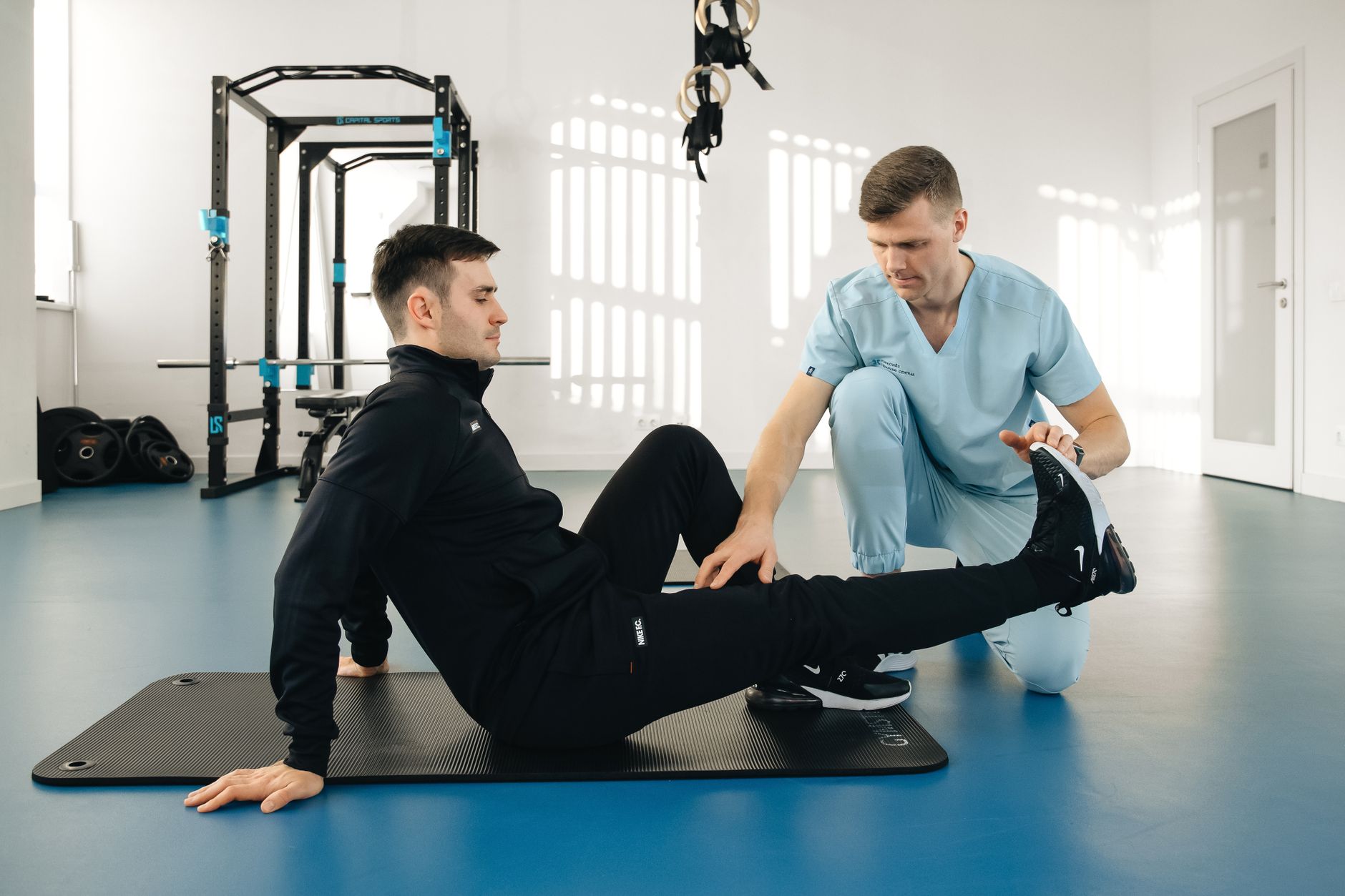 A therapist steadying a patient through a seated exercise during a rehabilitation session in a clinic