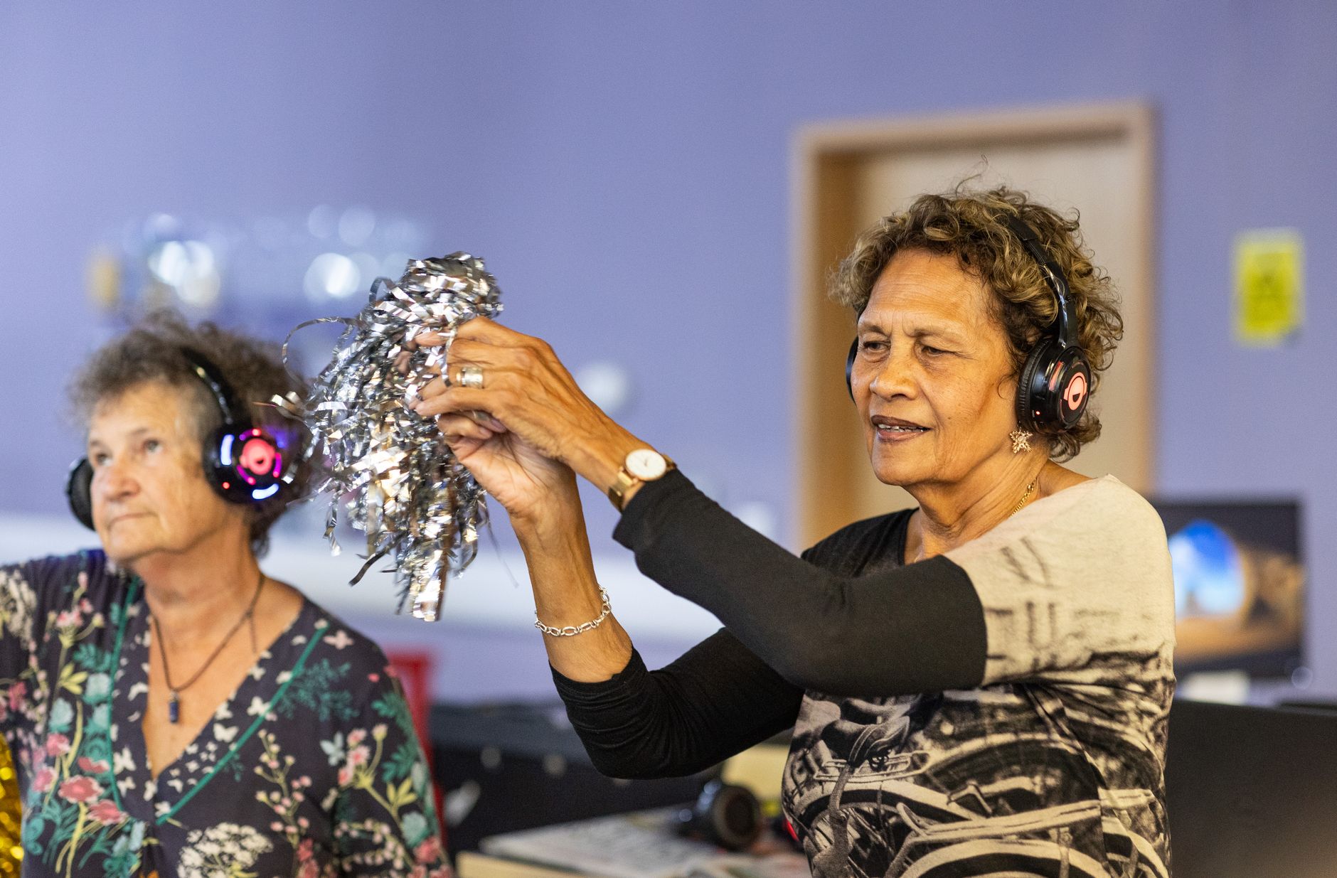 Two older women dancing to music through headphones in a care setting