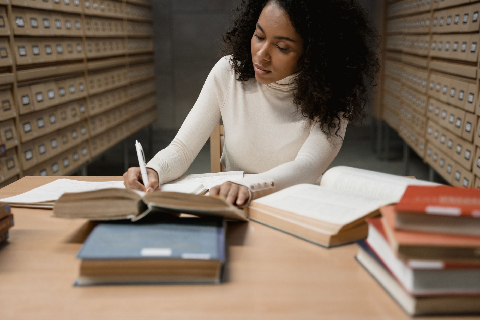 A researcher working through printed sources and taking notes at a library desk