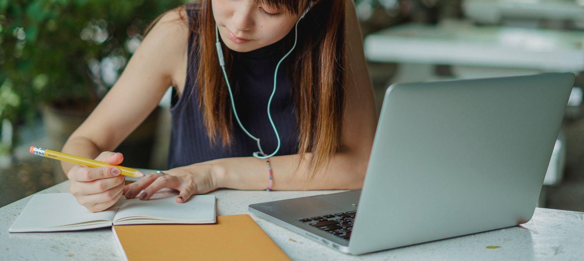 A student taking handwritten notes beside an open laptop at a desk