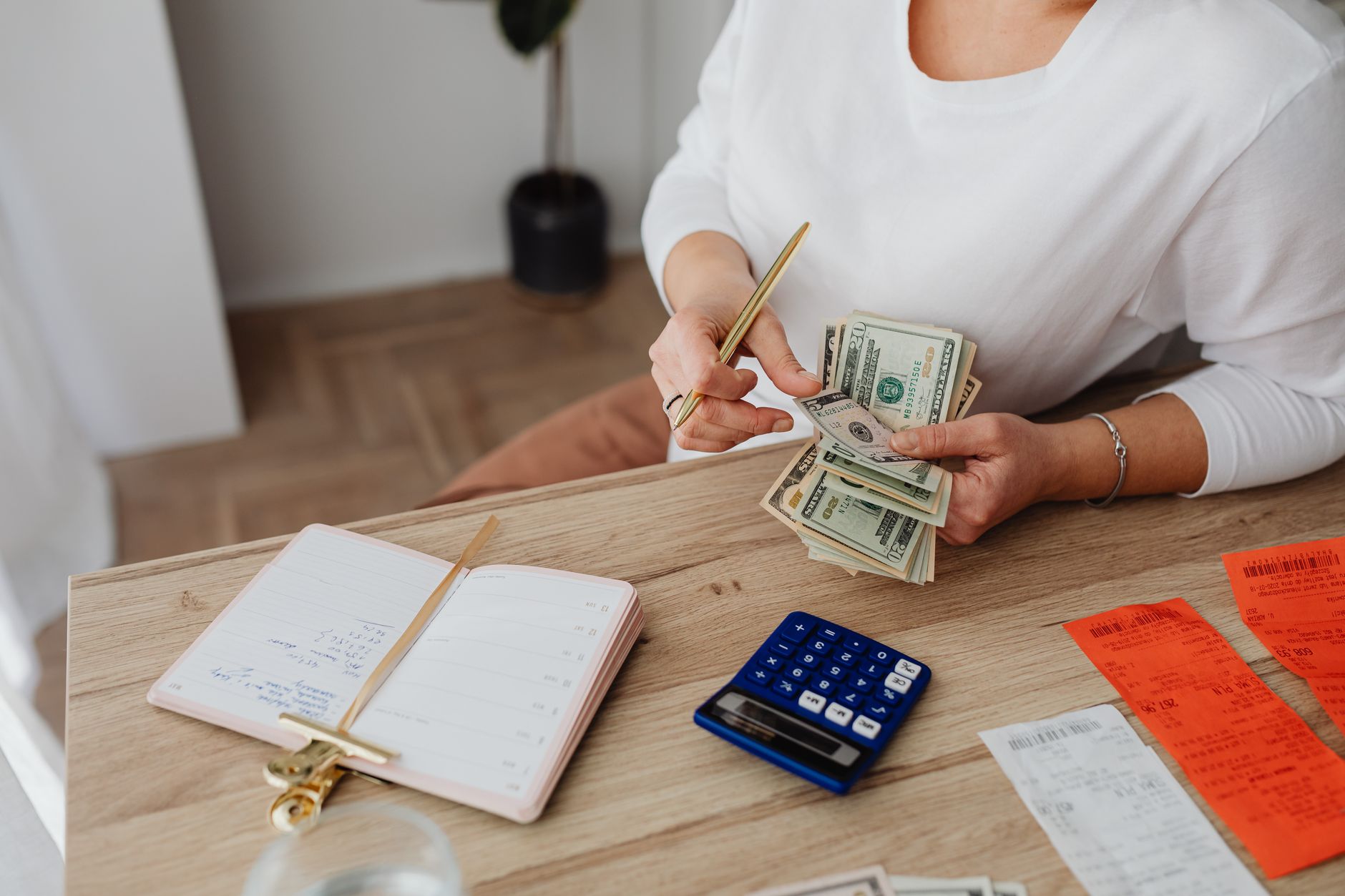 Someone working through bills and receipts at a desk with a calculator and cash